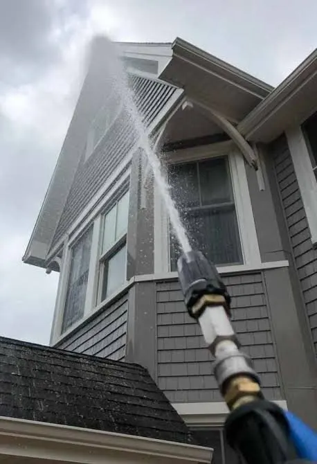 Soft washing spray cleaning siding and eaves from the ground.