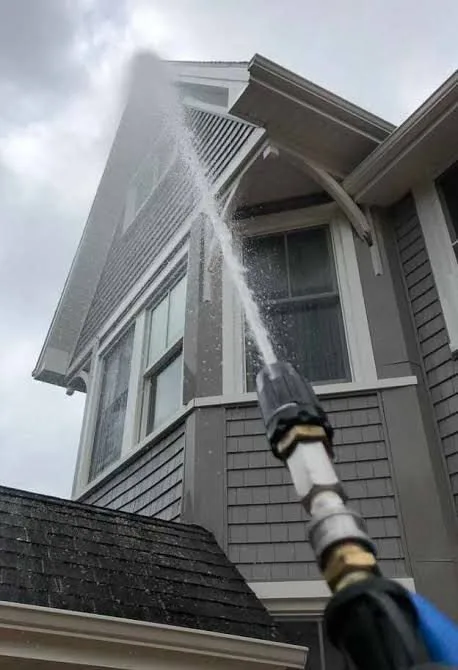 Soft washing spray cleaning siding and eaves from the ground.