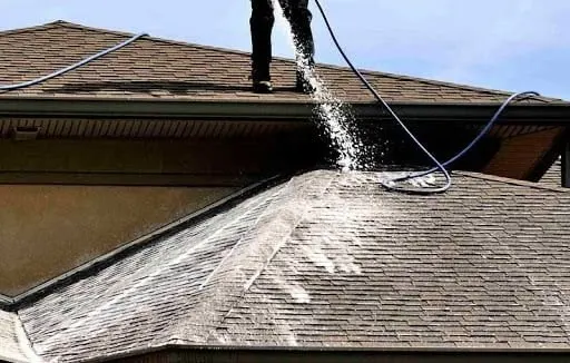 Low-pressure roof washing spray rinsing dark roof streaks from shingles.