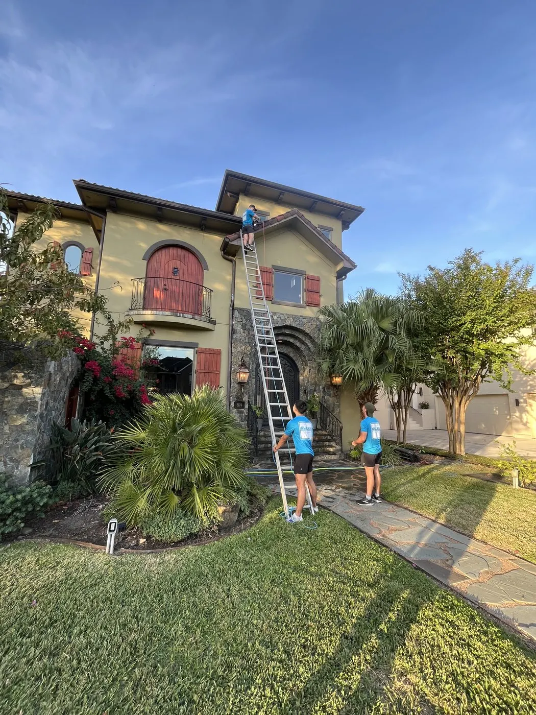 Two Gleam Clean technicians cleaning large exterior front windows with ladder and water-fed pole.