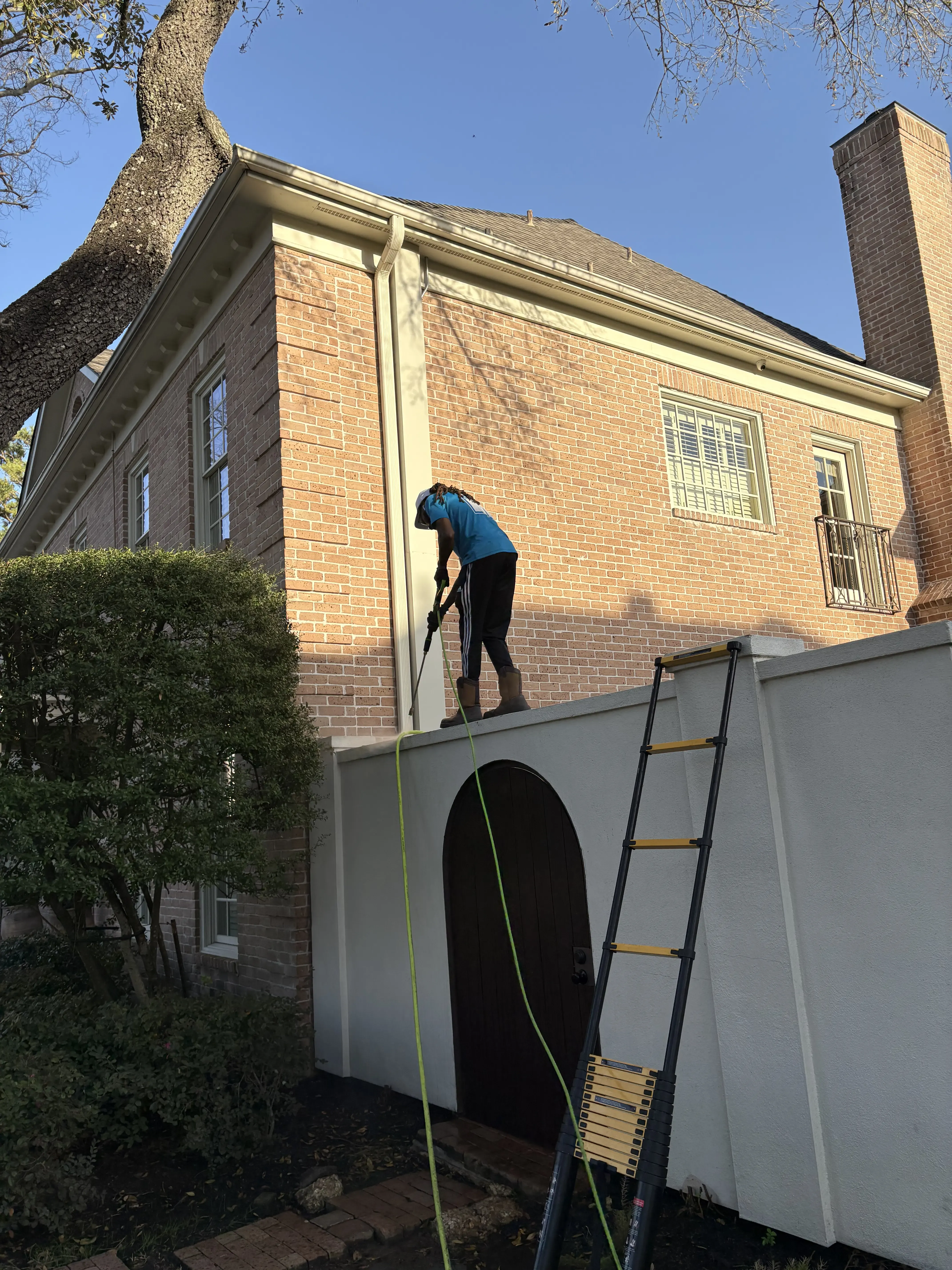 Gleam Clean technician using a water-fed pole to clean the upper exterior of a two-story brick home